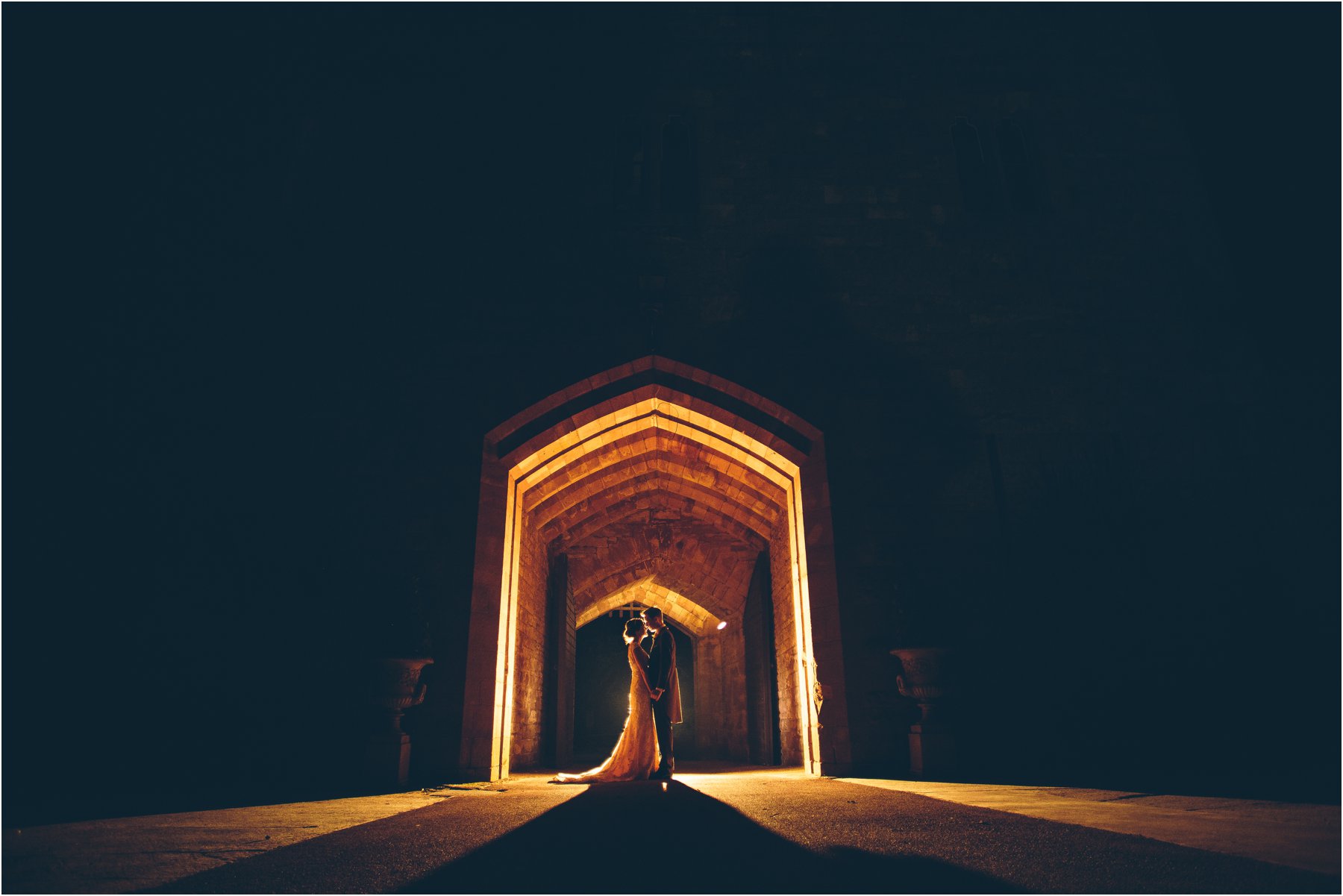 A stunning backlit photo of a bride and groom standing outside the entrance of Peckforton Castle taken by award winning wedding photographer The Crawleys