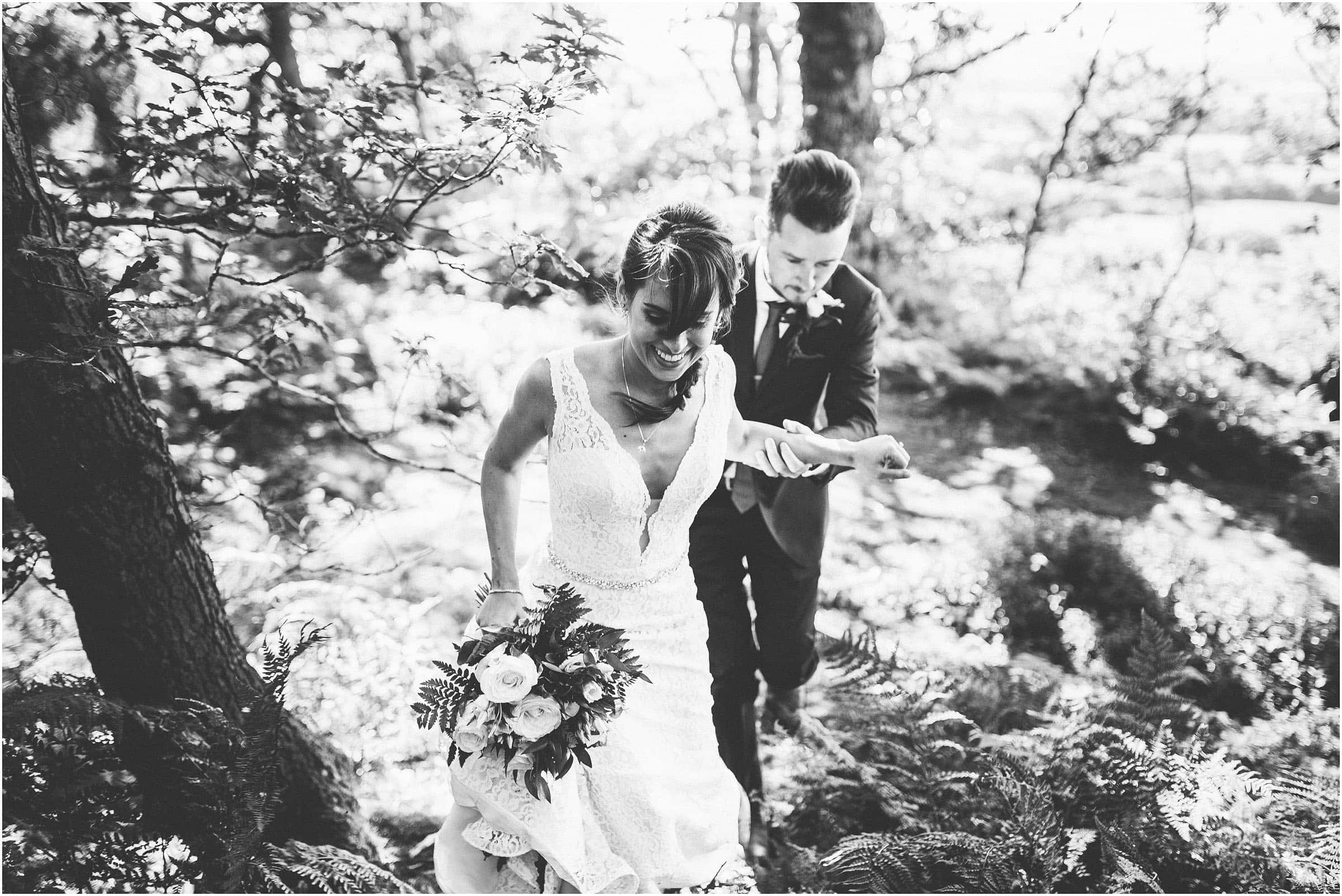 A black and white photo of a happy couple walking through the woods after their wedding ceremony at Peckforton Castle
