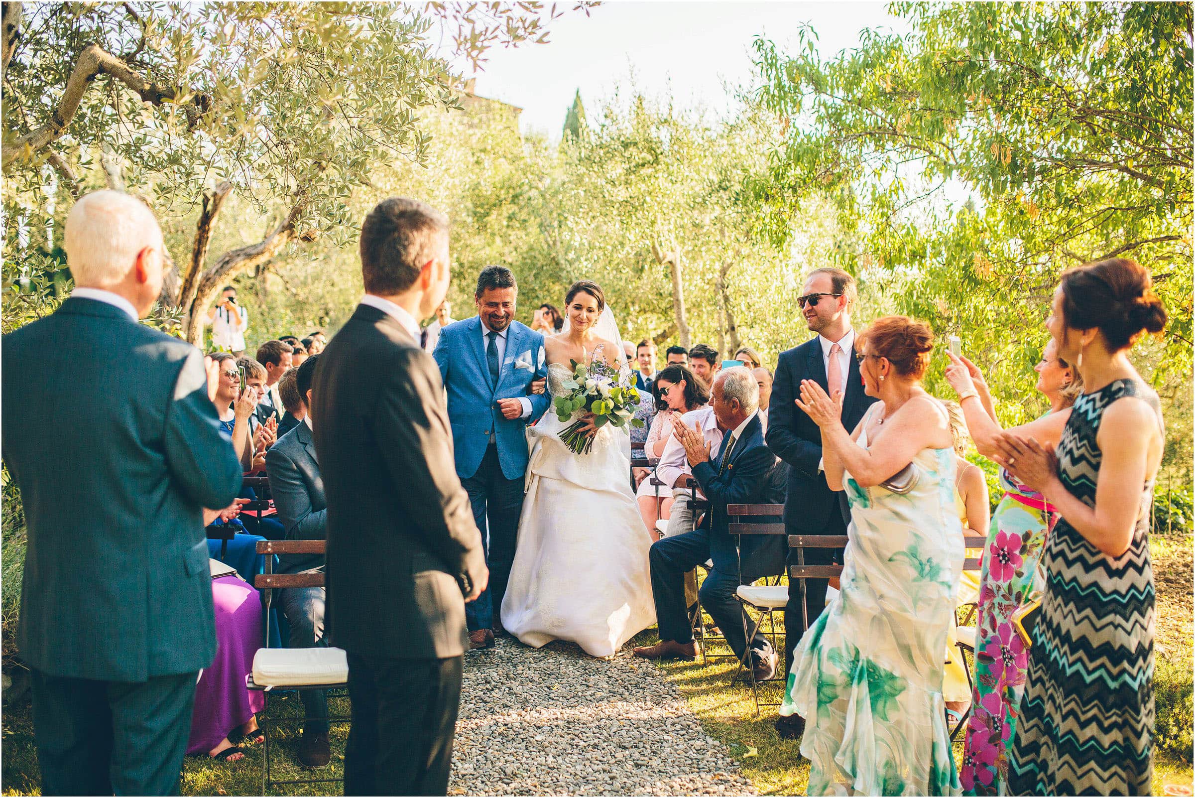 The bride makes her way down the aisle at Castello di Vicarello in Tuscany as her groom stands and watches