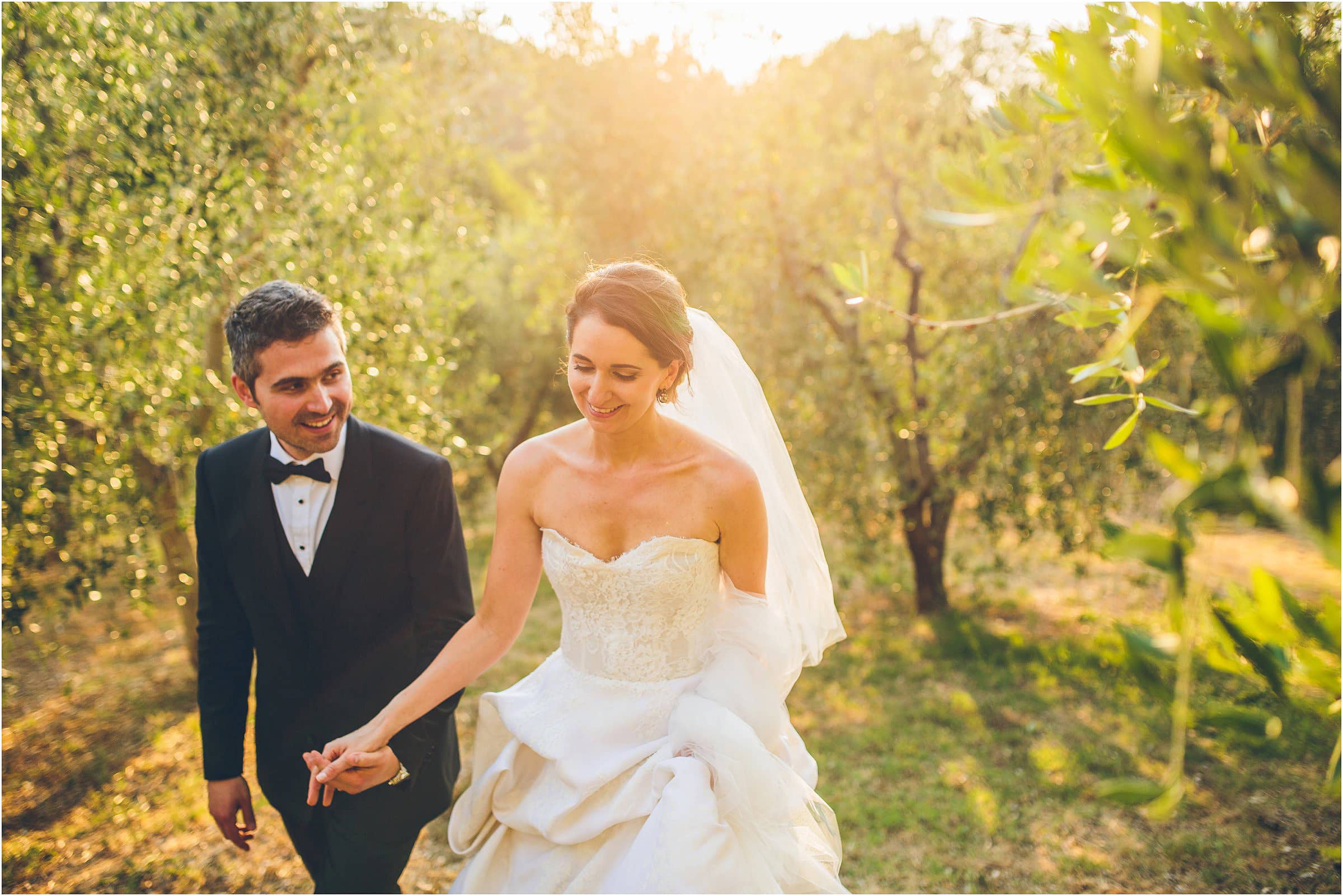 The happy couple hold hands and walk through the trees at Castello di Vicarello in Tuscany