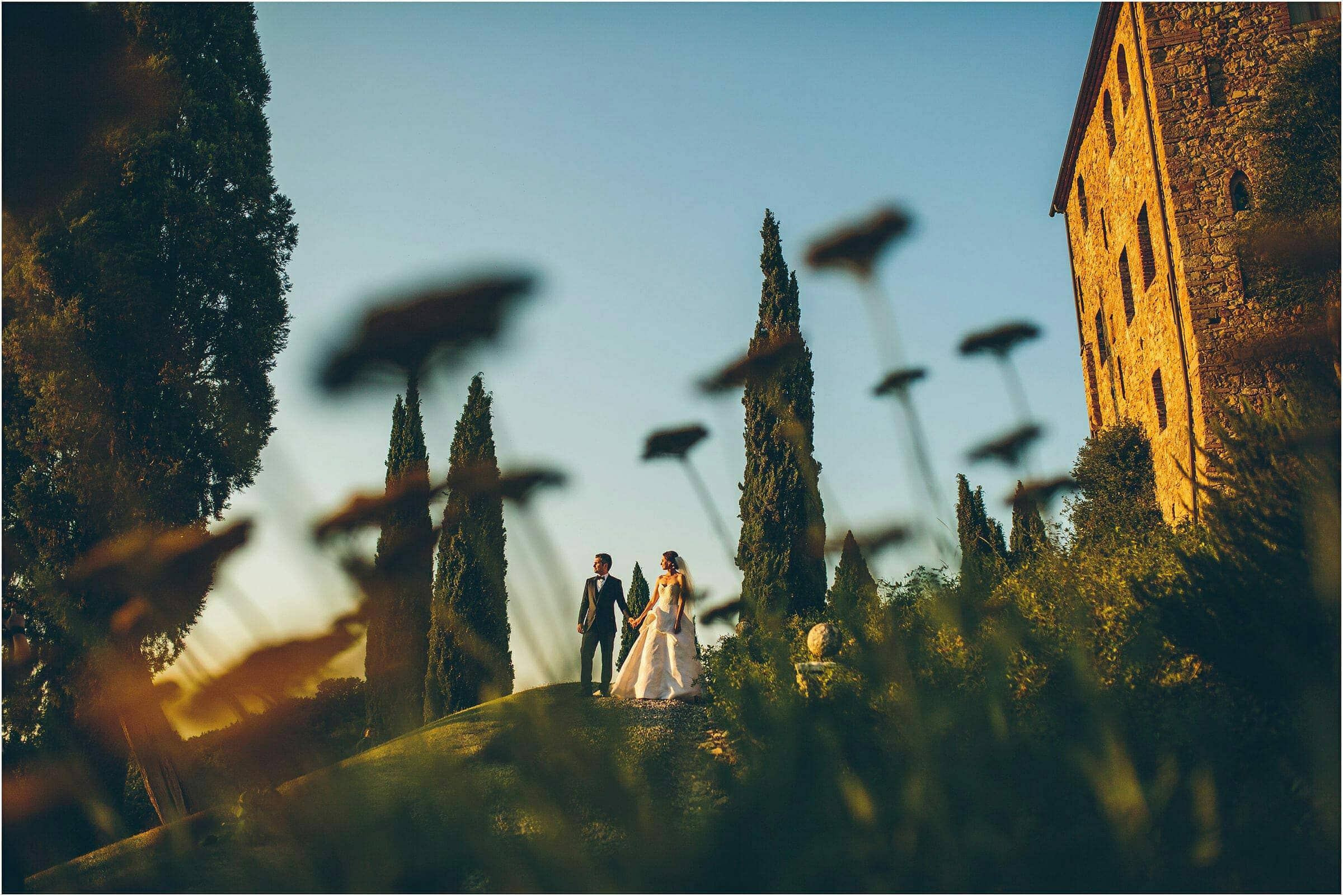 The bride and groom outside Castello di Vicarello on their destination wedding photographed through the plants in the sunset