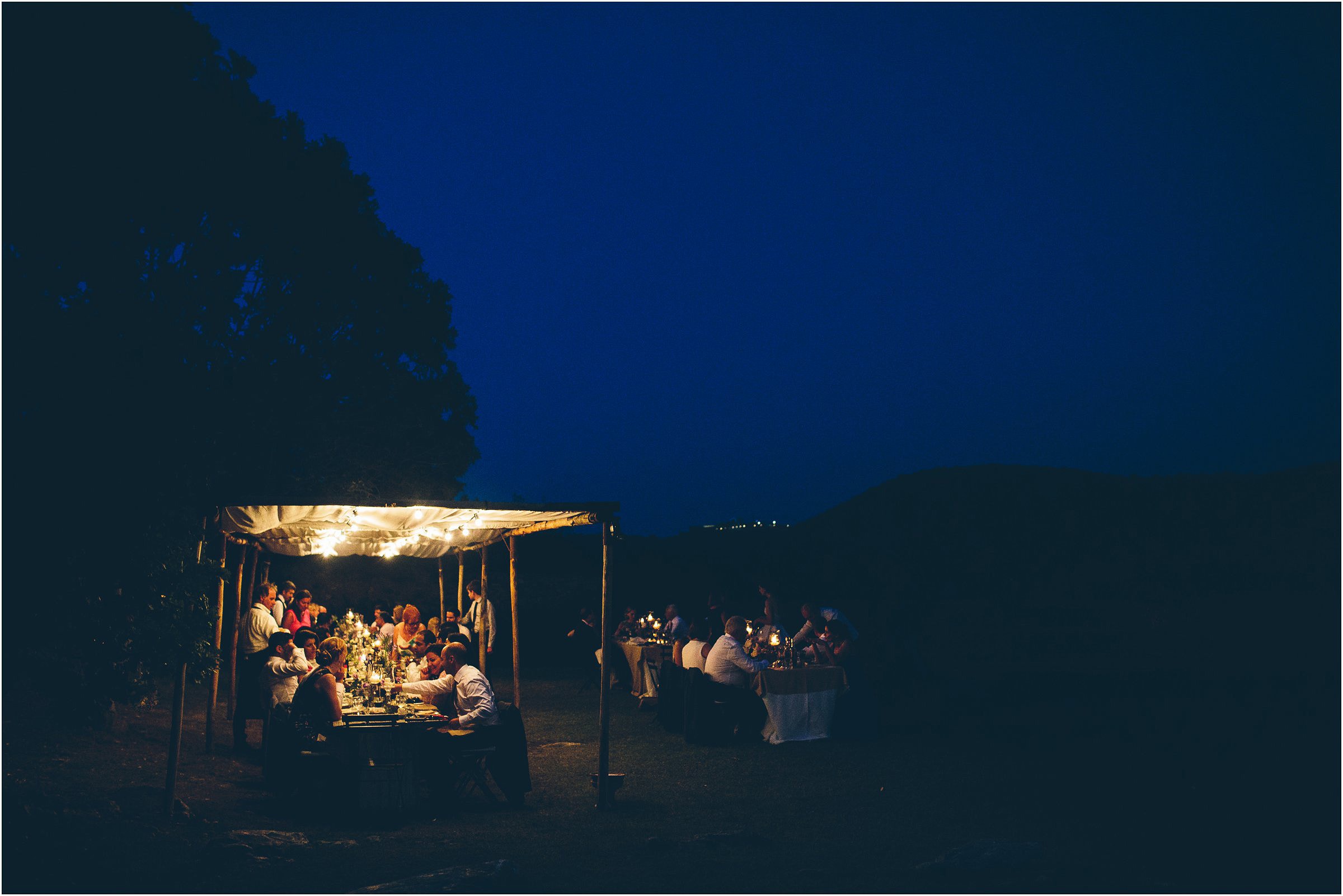 Wedding guests eating outdoors under lights at Castello di Vicarello in Tuscany