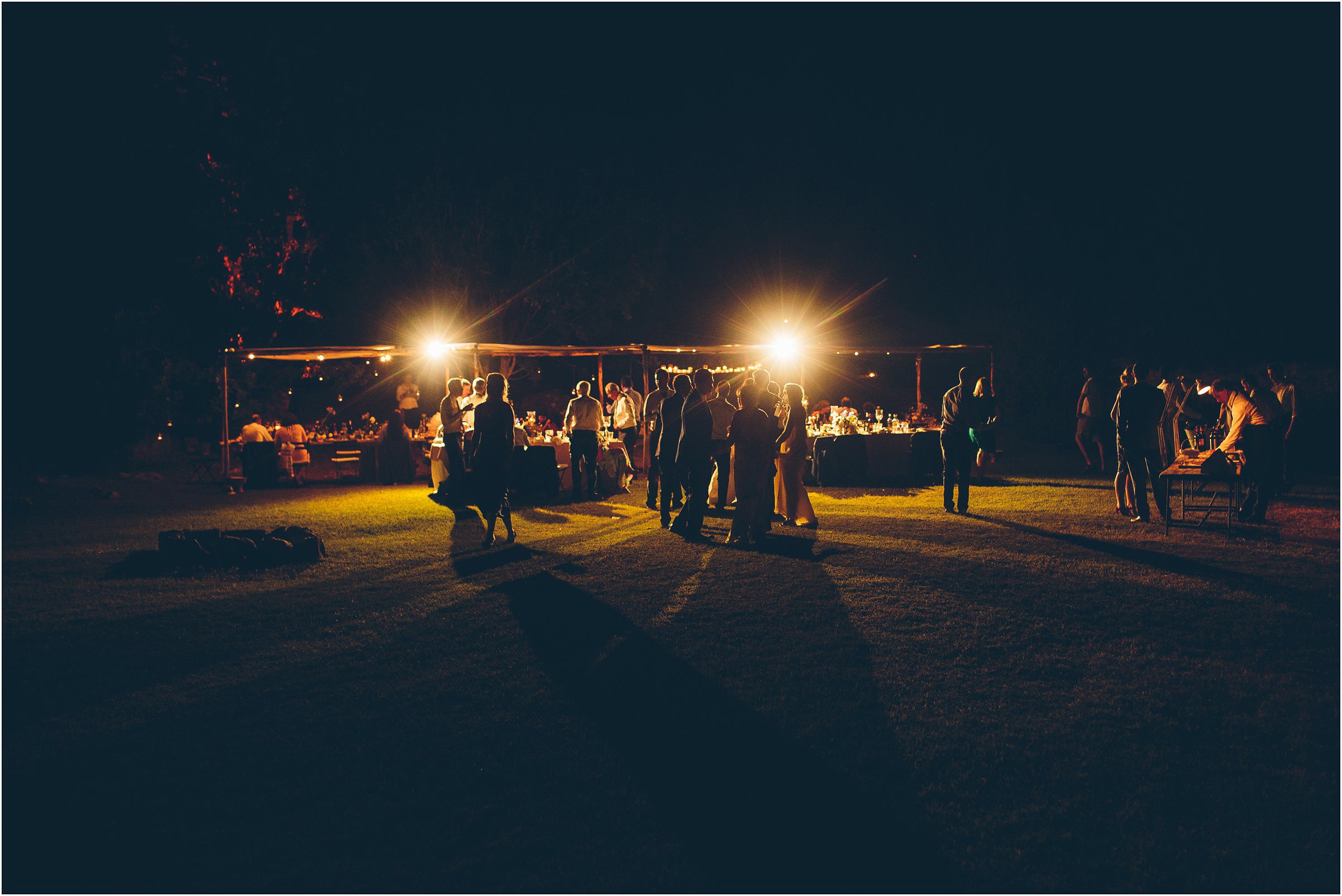 Guests at a destination wedding in Tuscany gather in the soft light of their outdoor party in the night.