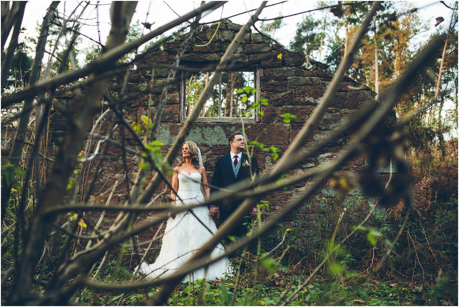A bride and groom take their wedding portraits in front of an abandoned, rustic outbuilding on the estate of Peckforton Castle.