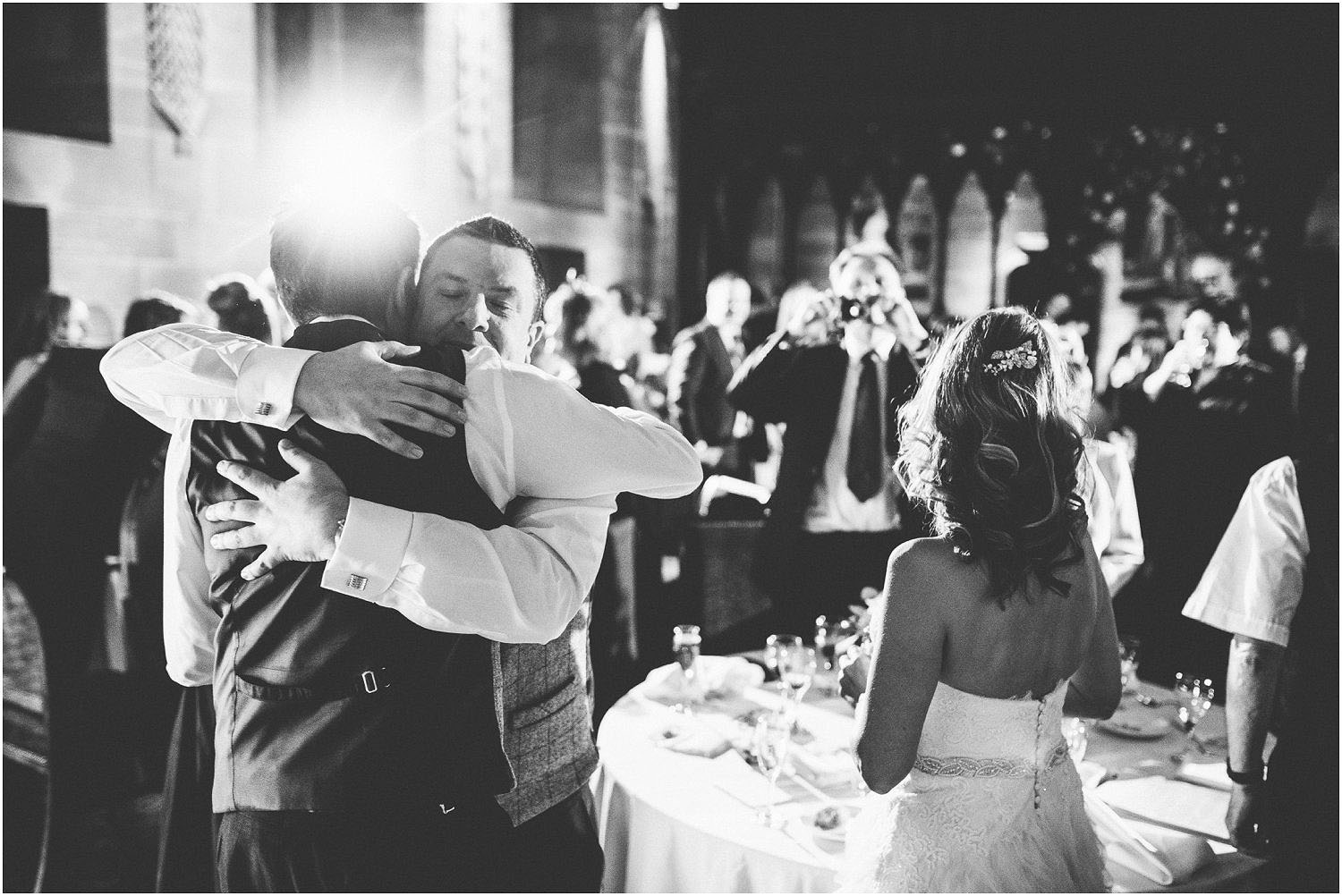 A black and white photo of a bride and groom hugging wedding guests at their wedding breakfast in Peckforton Castle