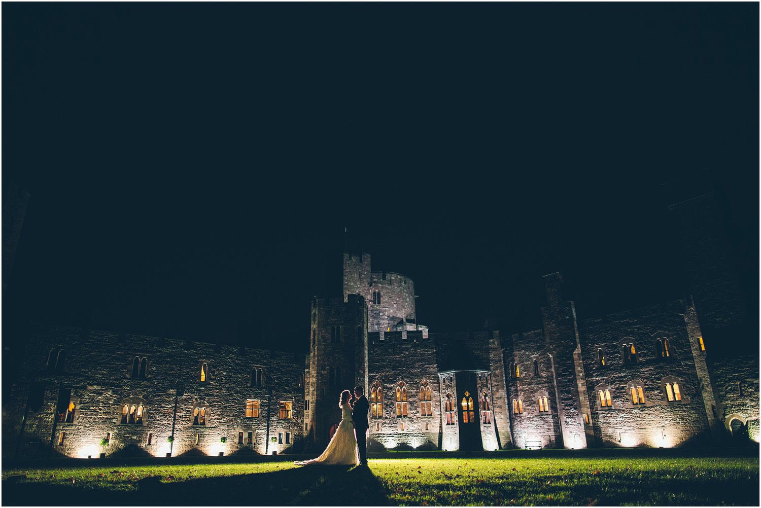 A dramatic backlit photo of a bridge and groom on their wedding day in front of Peckforton Castle takeb by The Crawleys