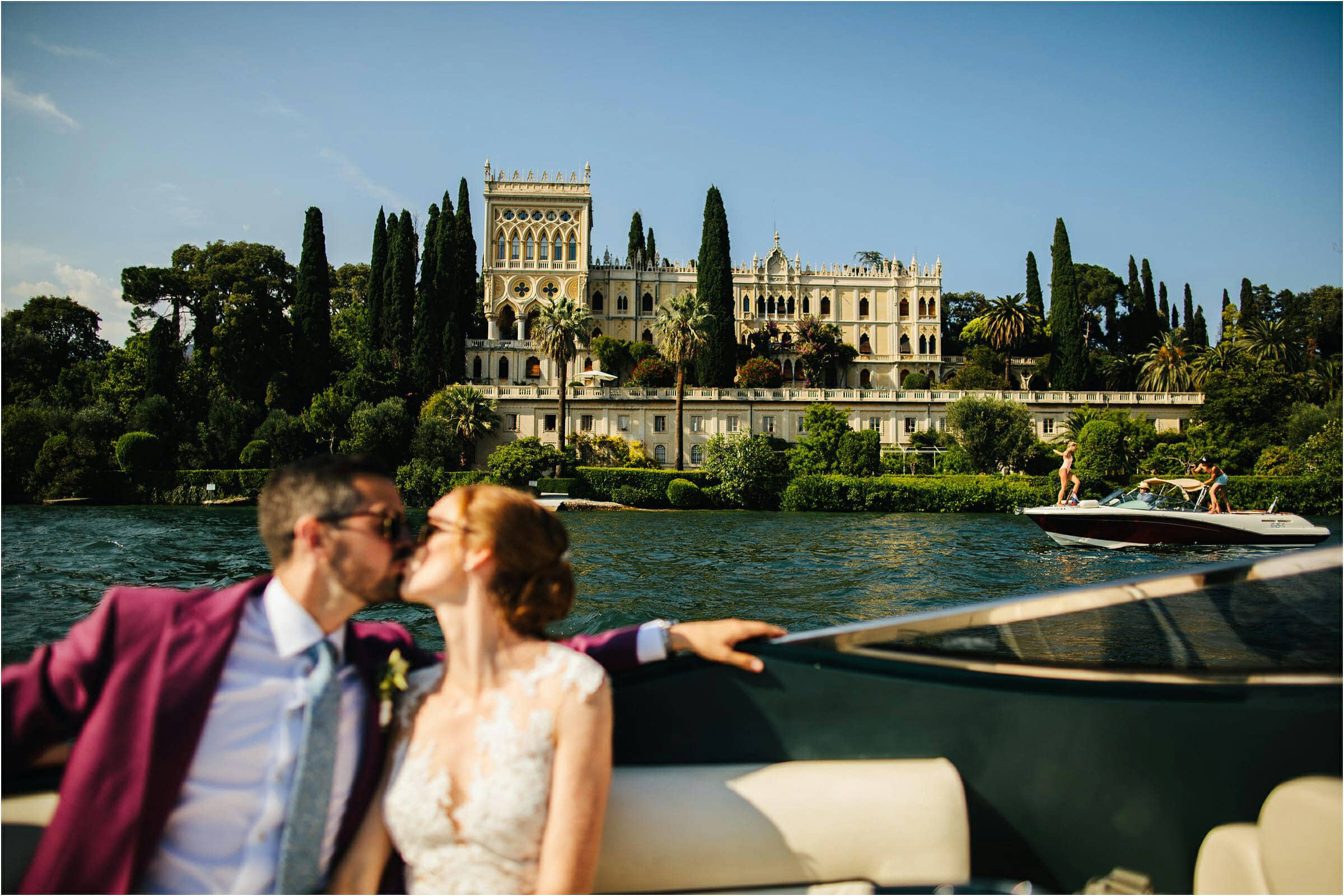bride and groom in a Riva kissing in front of Isolators del Garda in Italy
